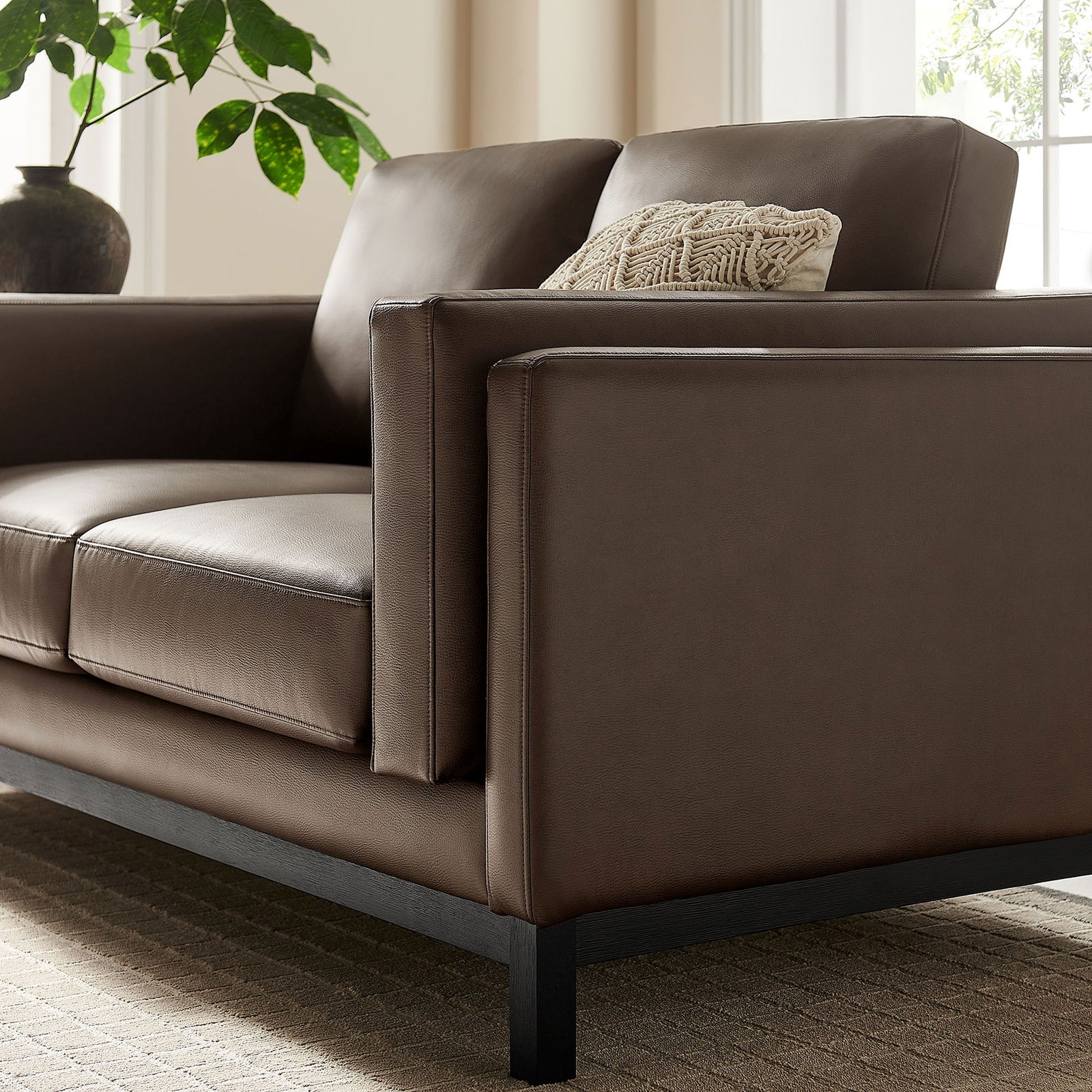 Loveseat arm styled with a textured accent pillow, espresso vegan leather, and black wood base in a bright room || EEI-7336-ESP || detail_room