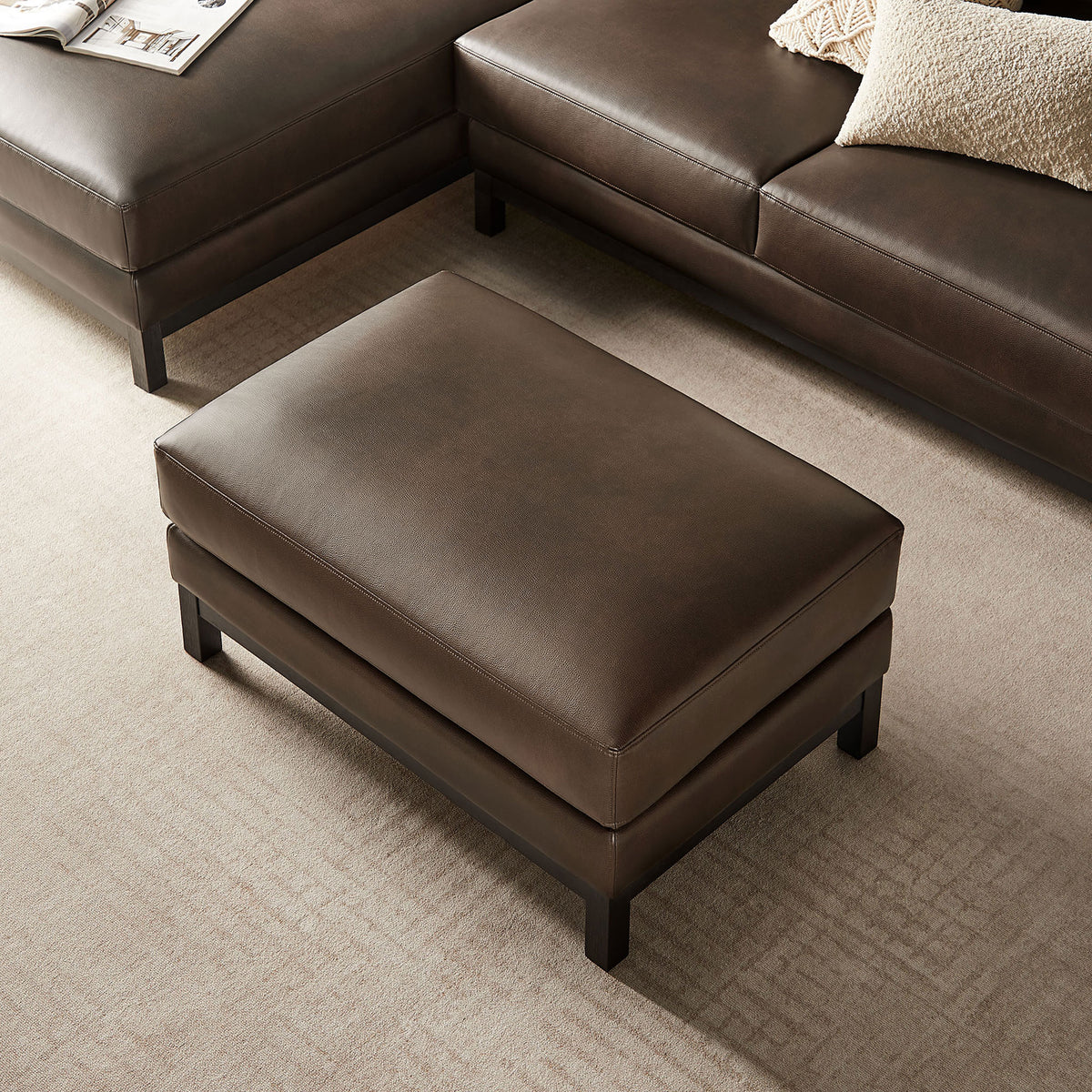 Roscoe espresso ottoman centered in living room grouping with matching sectional and throw pillow. || EEI-7338-ESP || top_angle_room