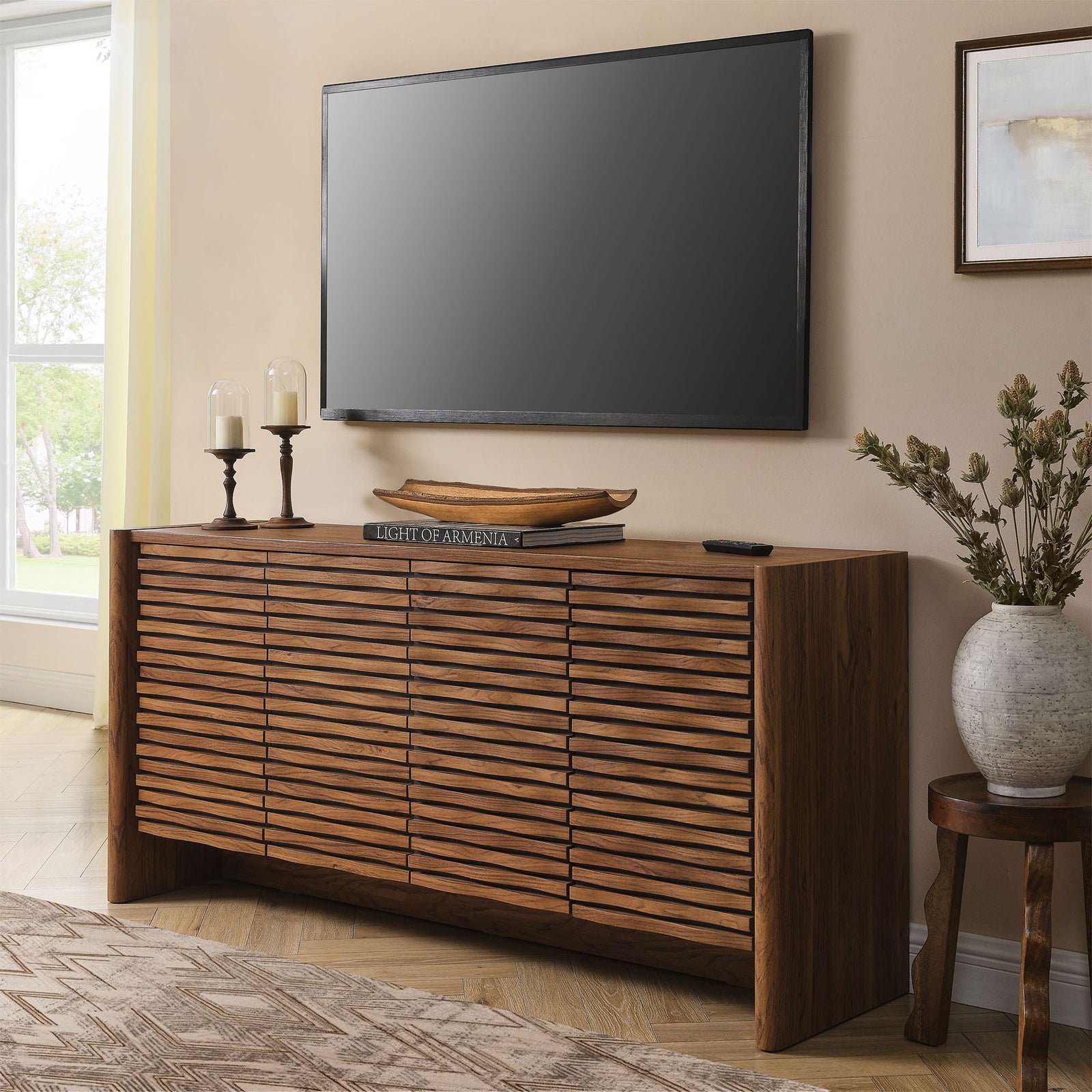 Walnut sideboard with sculpted doors used as a media console beneath a wall-mounted television || EEI-7346-WAL || front_angle_room