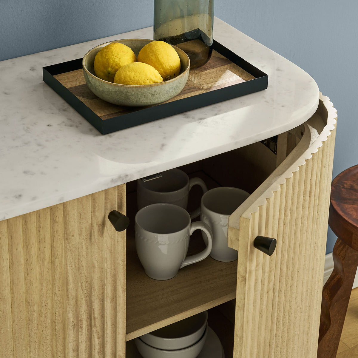 Marble-topped fluted wood cabinet in use, with door open to reveal neatly organized mugs and serveware inside || EEI-7354-NAT || storage_open_room