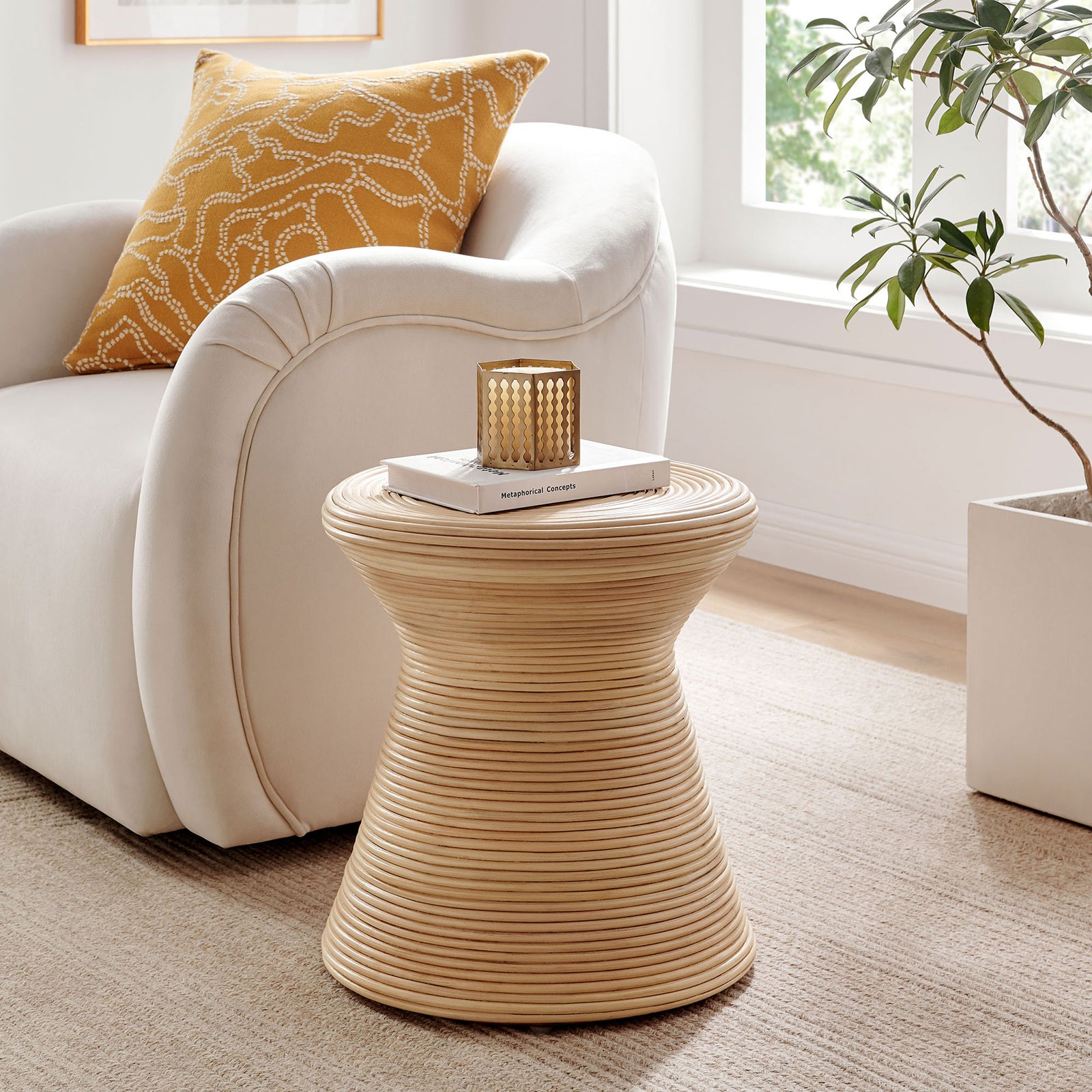 Natural rattan hourglass side table beside a plush sofa, adding organic warmth to a bright modern living room || EEI-7360-NAT || front_angle_room