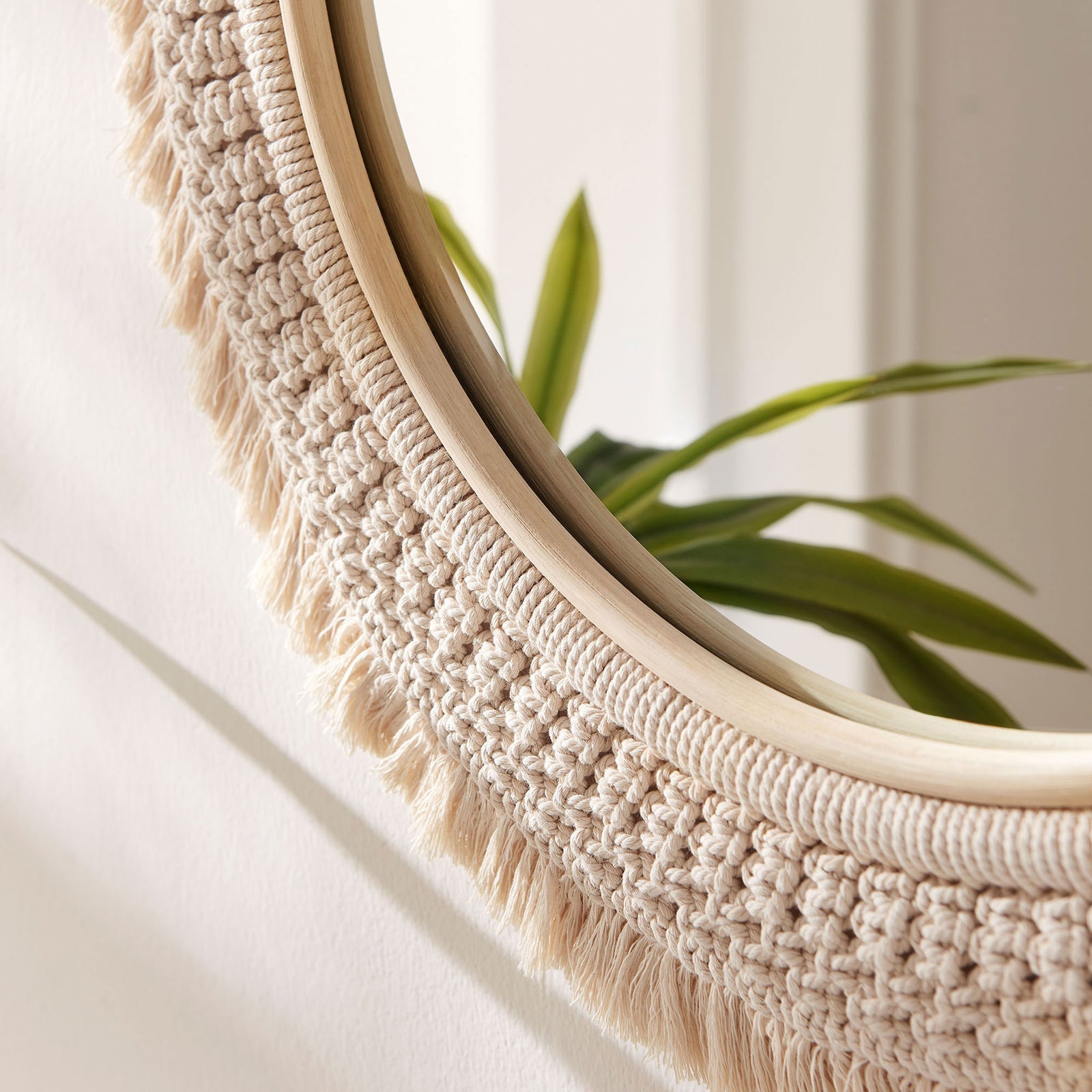 Macrame fringe and rattan frame catching natural light, styled on a bright wall with greenery for a relaxed feel. || EEI-7367-NAT || detail_room