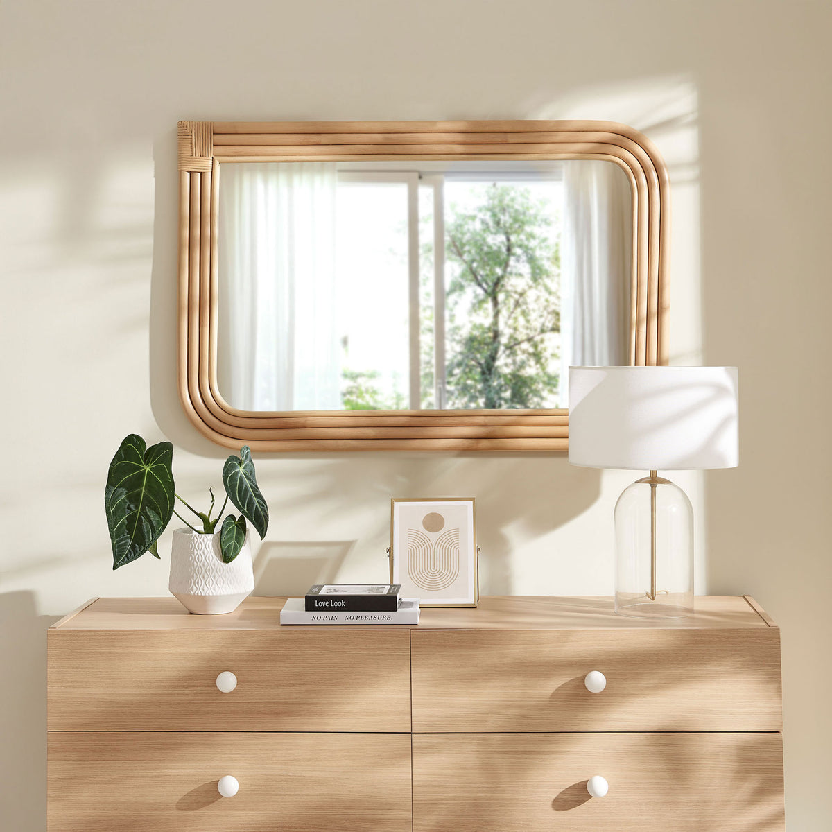 Corsica curved rectangle rattan mirror styled above a dresser in a bright, relaxed bedroom || EEI-7368-NAT || front_room