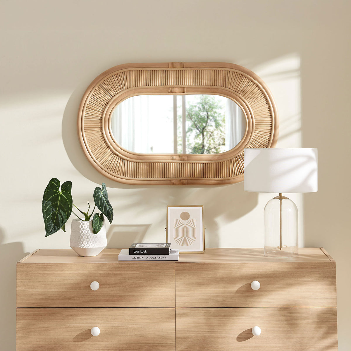 Oval rattan wall mirror mounted above a light wood dresser, adding natural warmth to a bright, modern room || EEI-7369-NAT || front_room