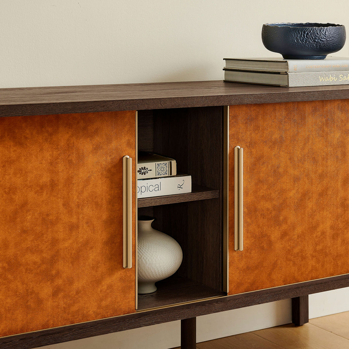 Styled display shows the media console in use, with sliding doors revealing decor and books on the center shelves. || EEI-7372-WAL-TAN || storage_open_room
