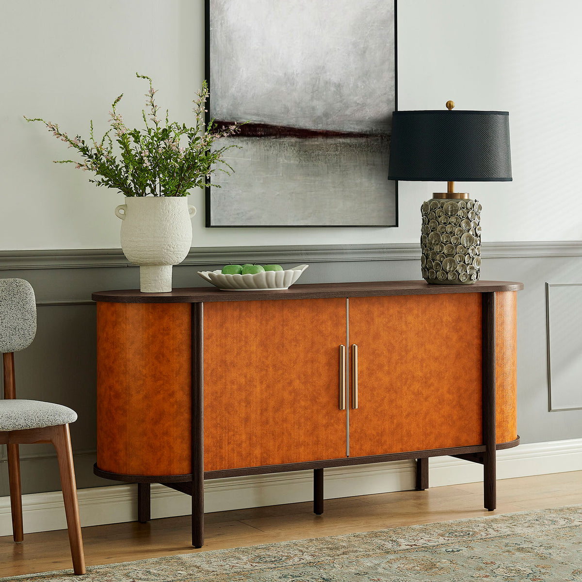 Walnut tan oval sideboard styled in a modern living room with artwork, lamp, and vase for a finished look || EEI-7373-WAL-TAN || front_angle_room