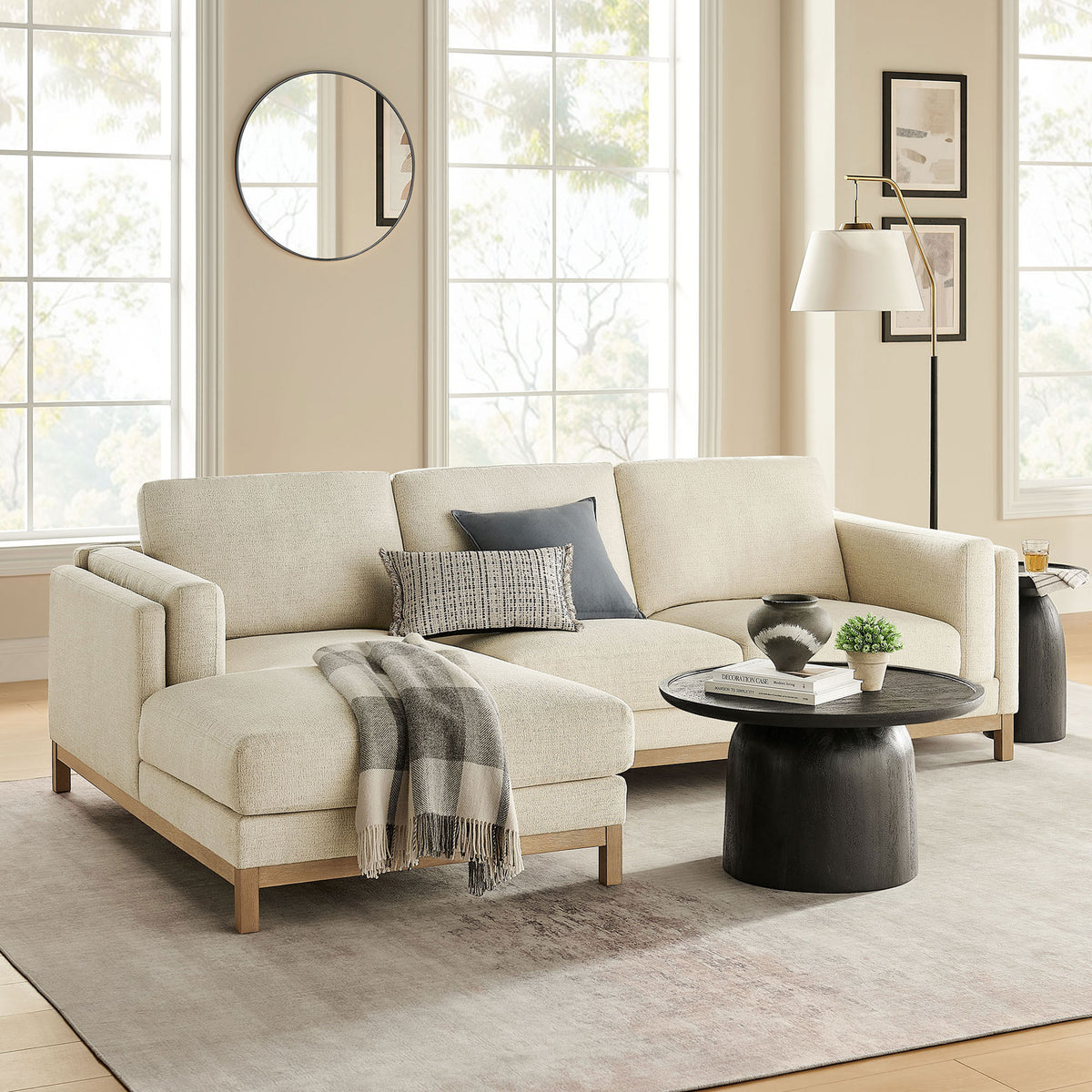 Ivory left-facing sectional in a bright living room, paired with a round black coffee table and neutral decor || EEI-7374-IVO || front_angle_room