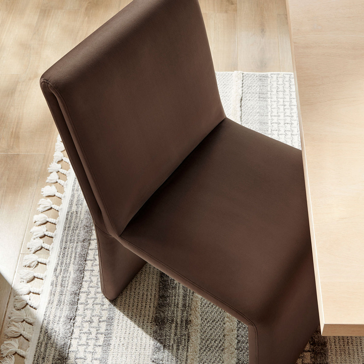 Emory chocolate velvet dining chair styled at a modern wood table, adding rich warmth against a neutral woven rug. || EEI-7384-CHB || front_angle_room