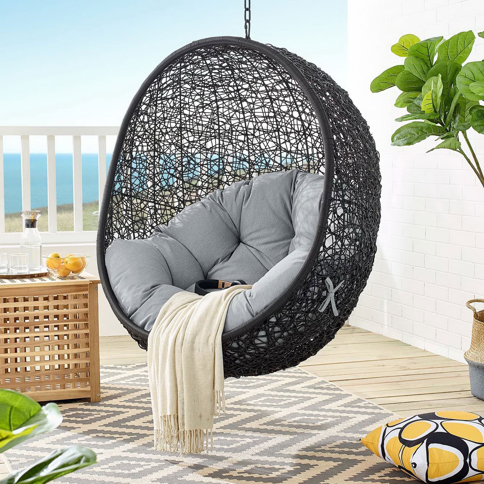 Gray cushion swing chair hangs from overhead on a bright balcony with ocean backdrop || EEI-739-GRY-SET || front_partial_room