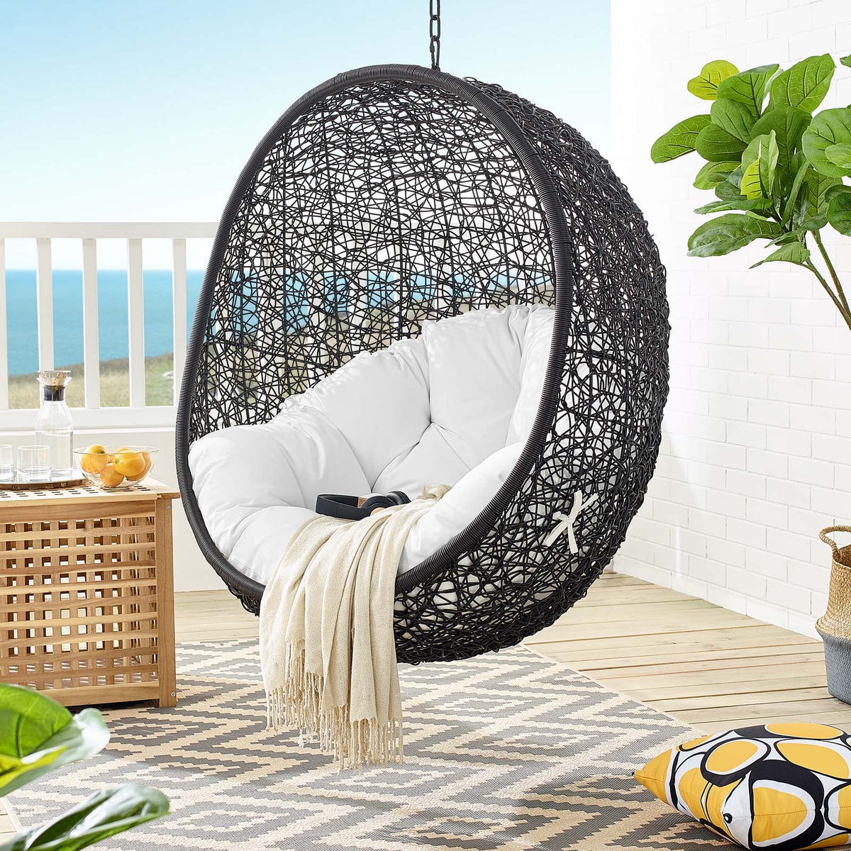 White cushion swing chair hangs freely on a seaside balcony with throw and coastal accents
