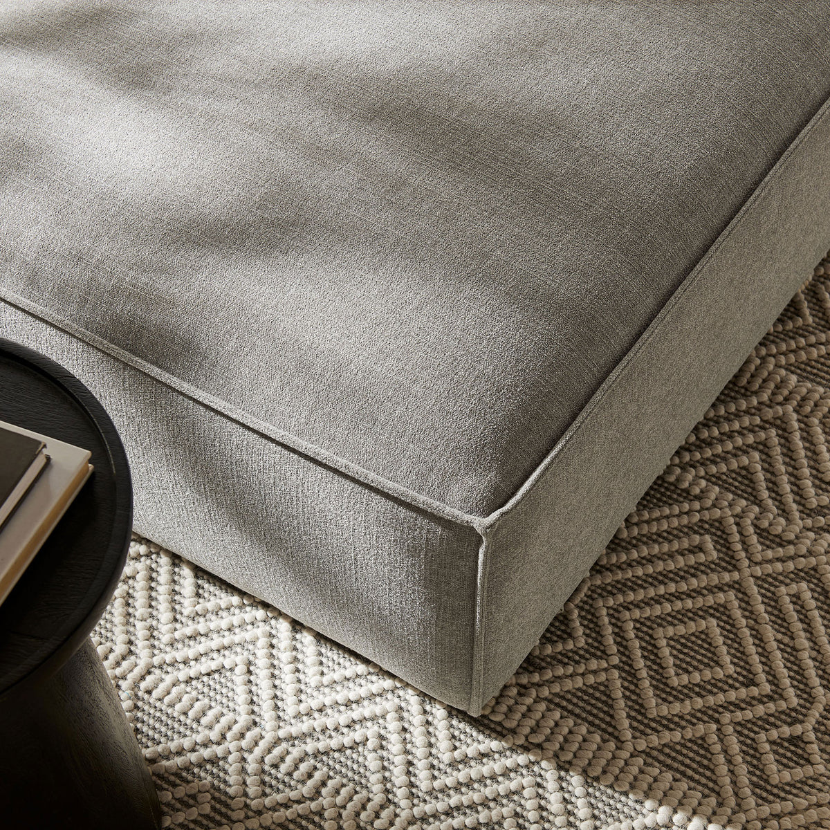 Pewter performance fabric ottoman styled on a patterned rug beside a modern black side table in a bright room || EEI-7401-PEW || detail_room