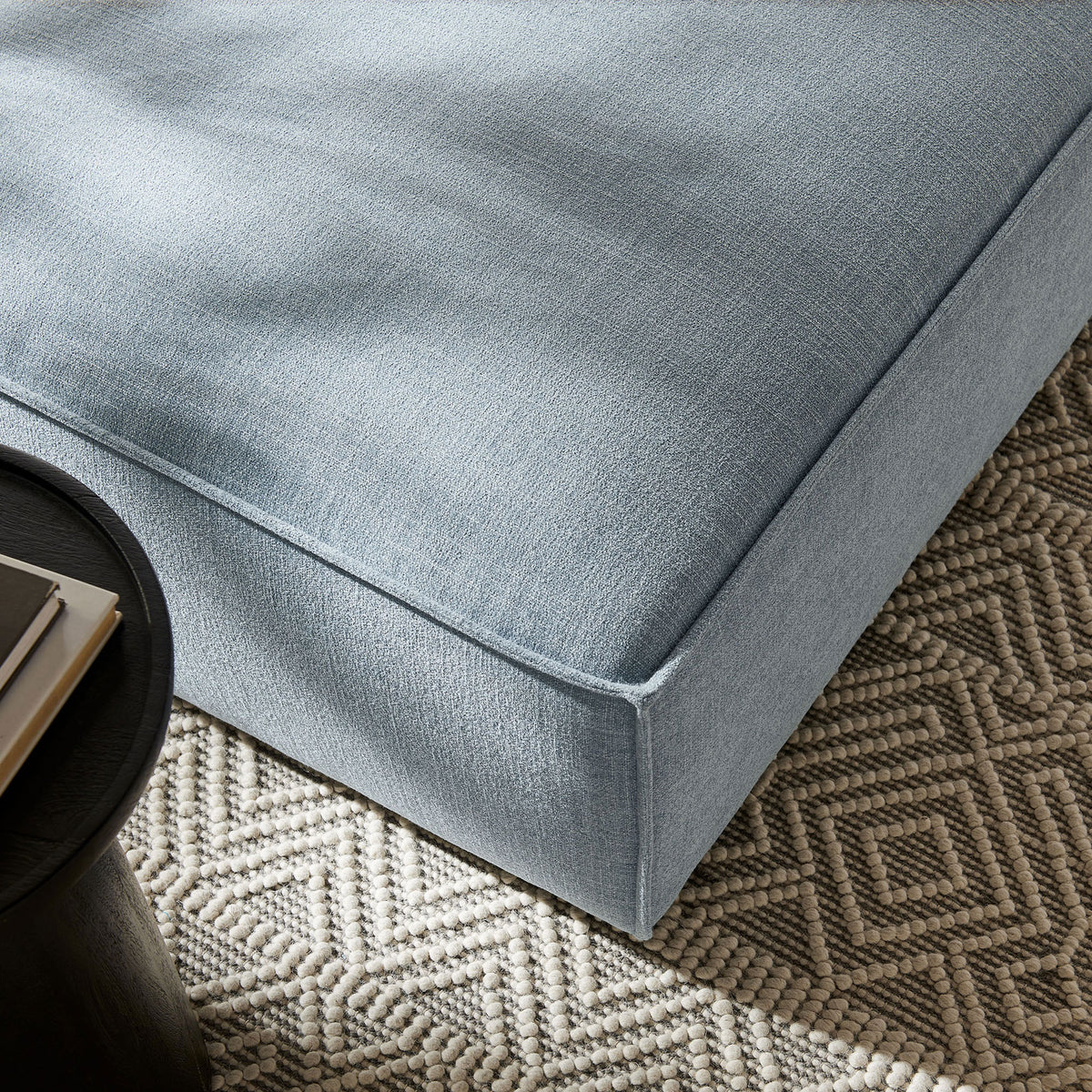 Sky blue ottoman pairs with a textured rug and side table, adding soft color and comfort to a modern living space || EEI-7401-SKY || detail_room