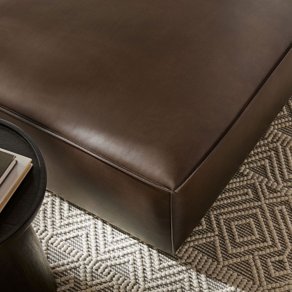 Espresso modular ottoman styled on a textured rug, bringing soft vegan leather comfort to your lounge. || EEI-7402-ESP || detail_room