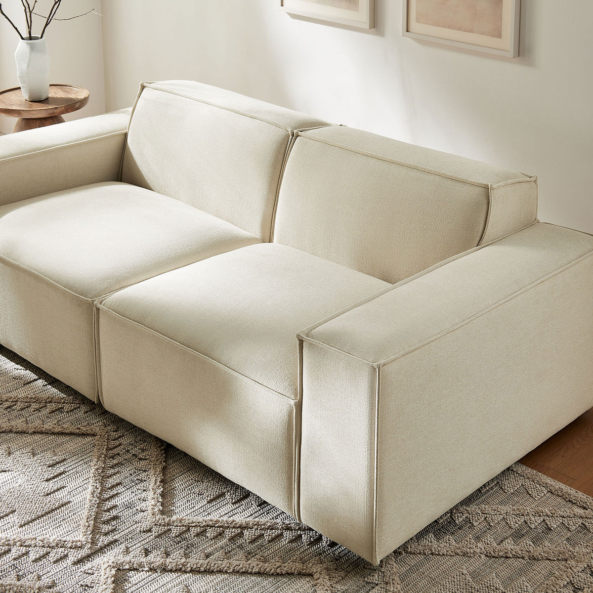 Performance fabric modular loveseat in ecru paired with wood accent tables and a patterned neutral area rug. || EEI-7403-ECR || front_angle_room