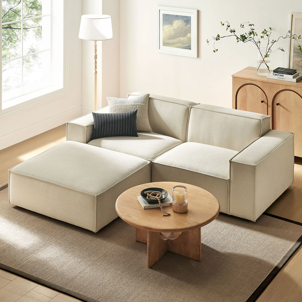 Restore ecru modular loveseat with ottoman creating a relaxed lounge setting in a bright room. || EEI-7405-ECR || front_angle_room