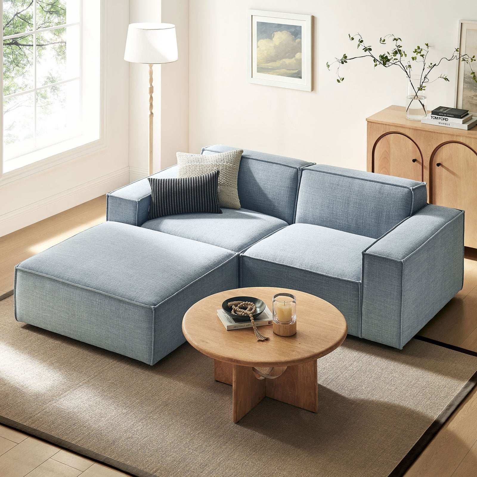 Sky blue modular loveseat with ottoman arranged in a modern living room with rug, lamp, and coffee table || EEI-7405-SKY || front_angle_room