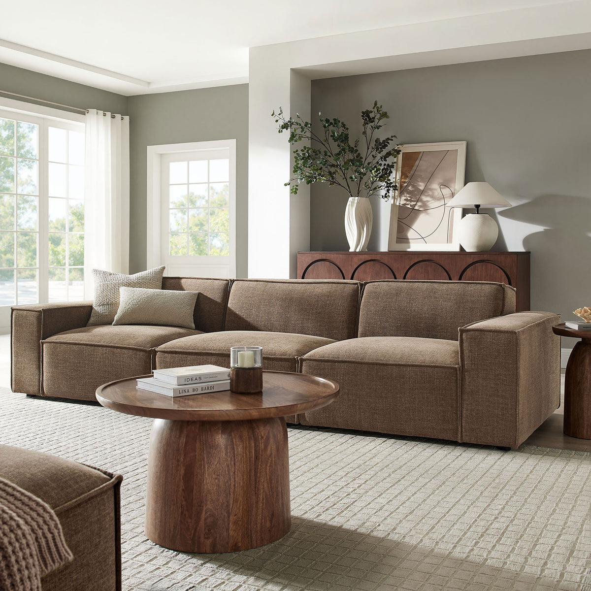 Spacious mocha modular sofa anchoring an airy living room with large windows and warm wood furnishings. || EEI-7407-MOC || front_angle_room