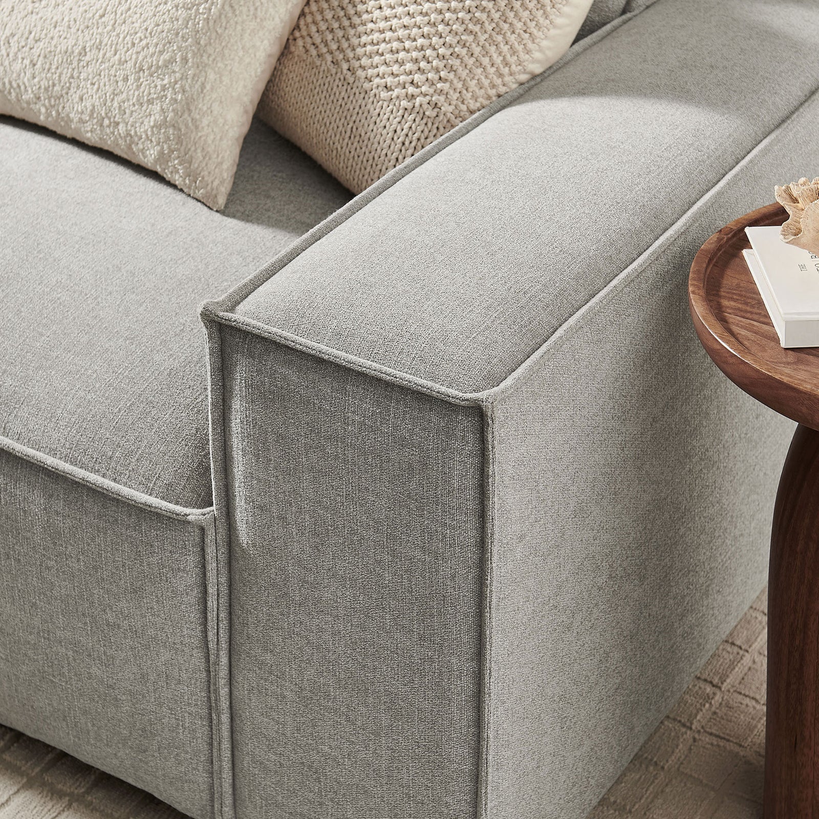 Wide track arm of the pewter modular sofa with French piping beside a round wood coffee table. || EEI-7407-PEW || detail_room