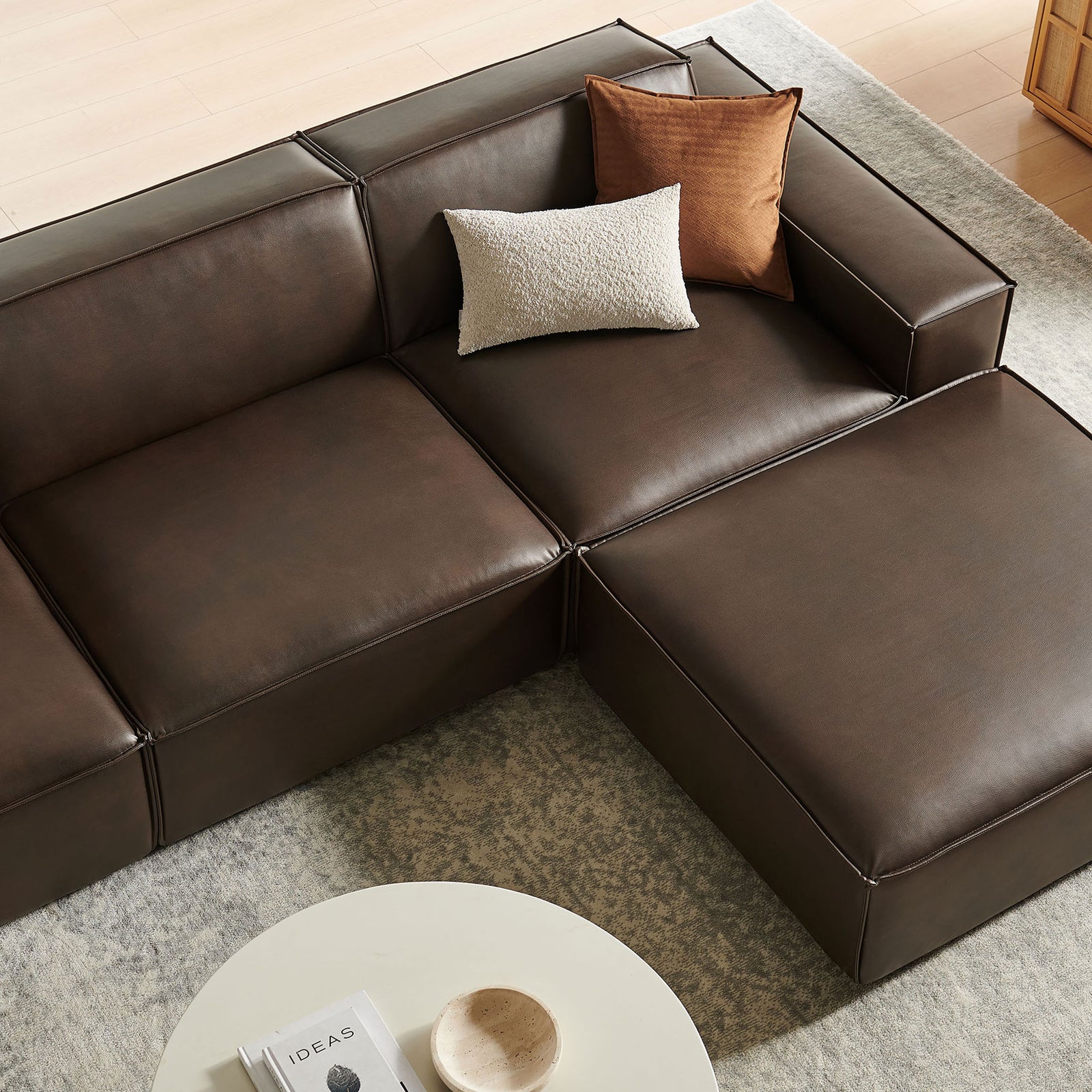 Espresso modular seating and ottoman on a light area rug beside a round coffee table and decor tray || EEI-7410-ESP || detail_room