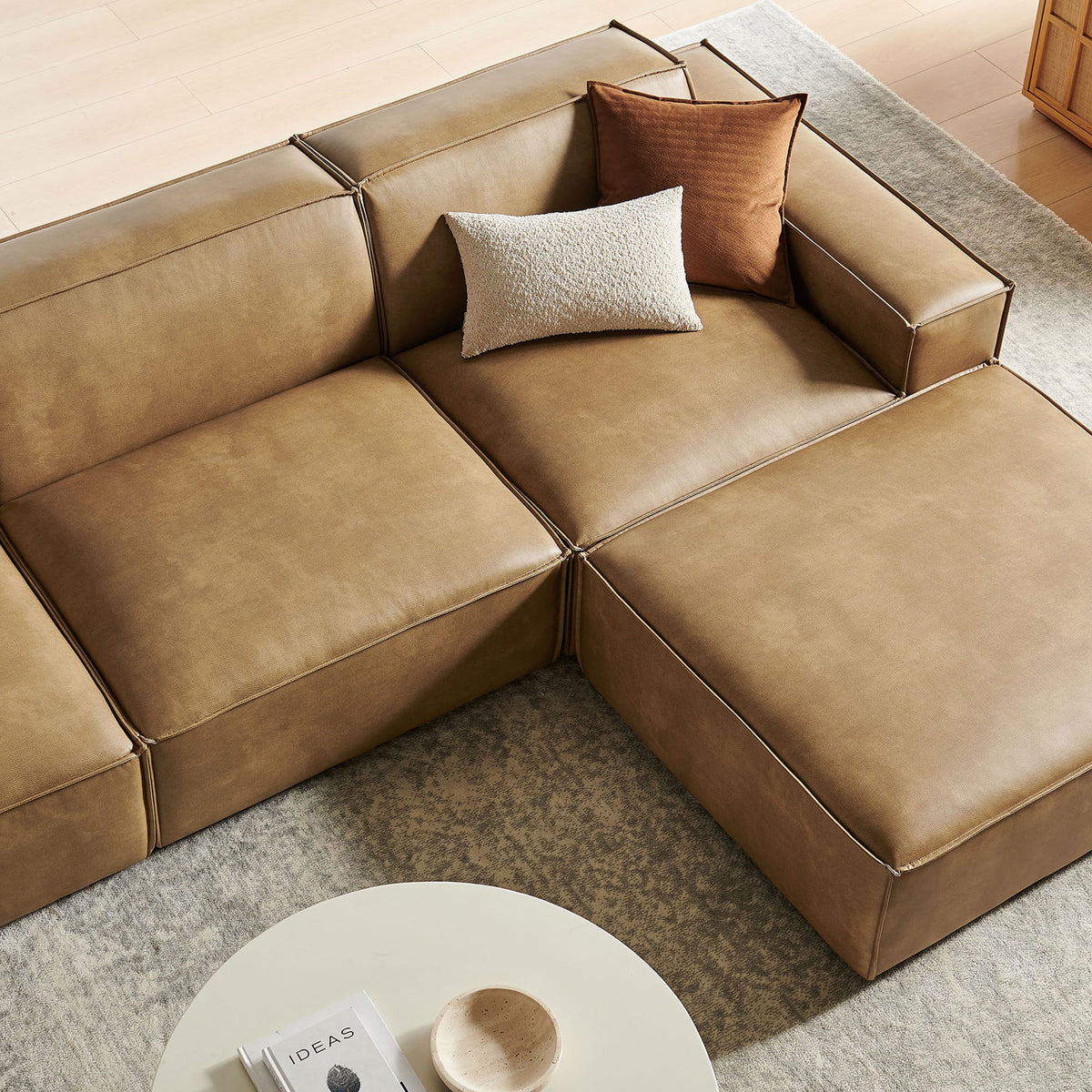 Cozy modular sofa in toast vegan leather styled with layered accent pillows and a plush area rug || EEI-7410-TST || detail_room