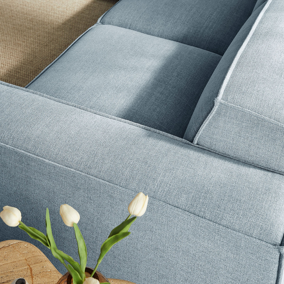Sky blue fabric sofa with subtle texture, tailored piping, and a cozy lounge feel beside a simple tulip arrangement || EEI-7411-SKY || detail_room