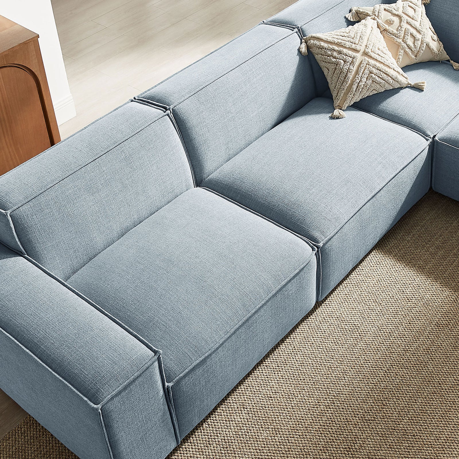 Soft sky blue sectional cushions with French piping and a textured throw pillow on a natural jute rug || EEI-7411-SKY || detail_room