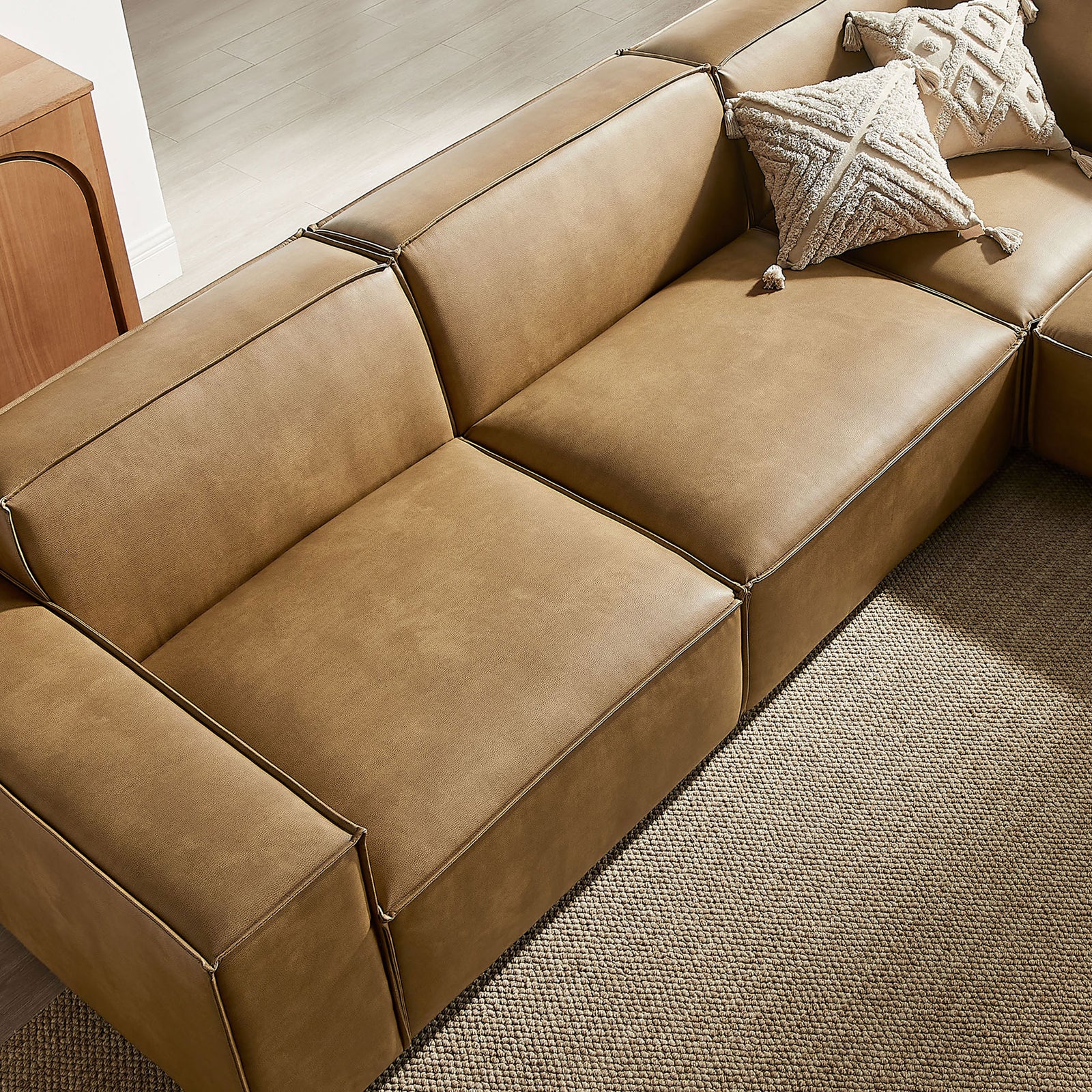 Sectional sofa seat in toast vegan leather styled with textured throw pillows on a neutral rug || EEI-7412-TST || detail_room