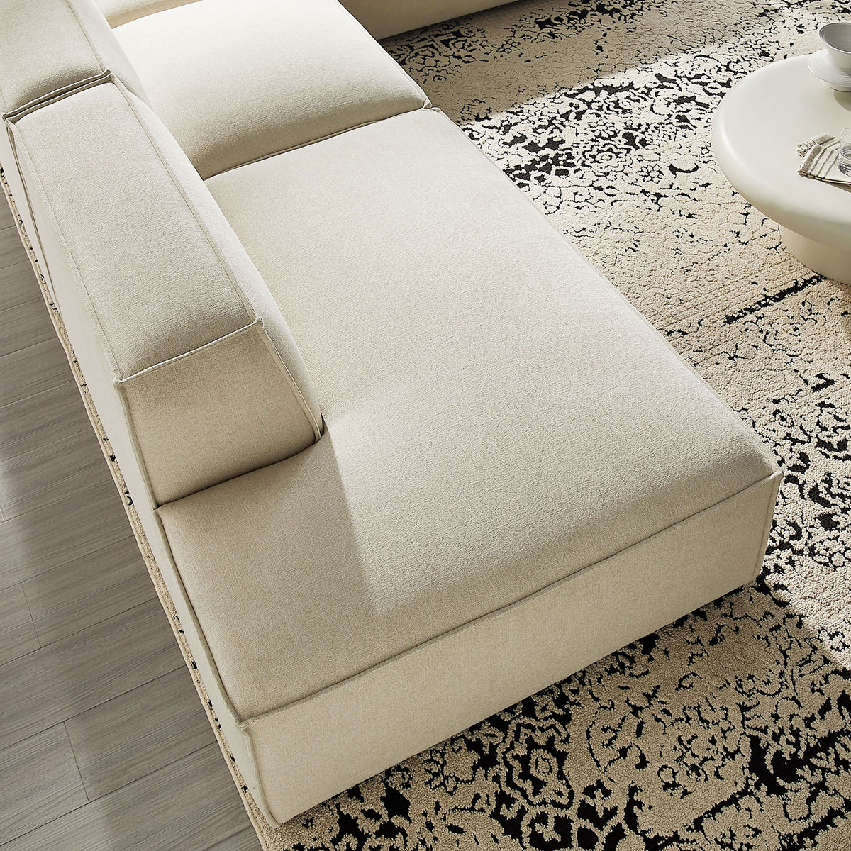 Generous chaise seat in ecru performance fabric layered over a patterned rug for relaxed lounging. || EEI-7413-ECR || detail_room