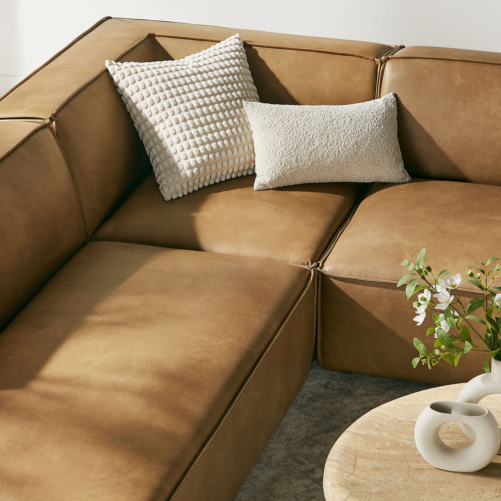 Toast vegan leather corner seat styled with textured cream pillows and fresh greenery || EEI-7416-TST || detail_room