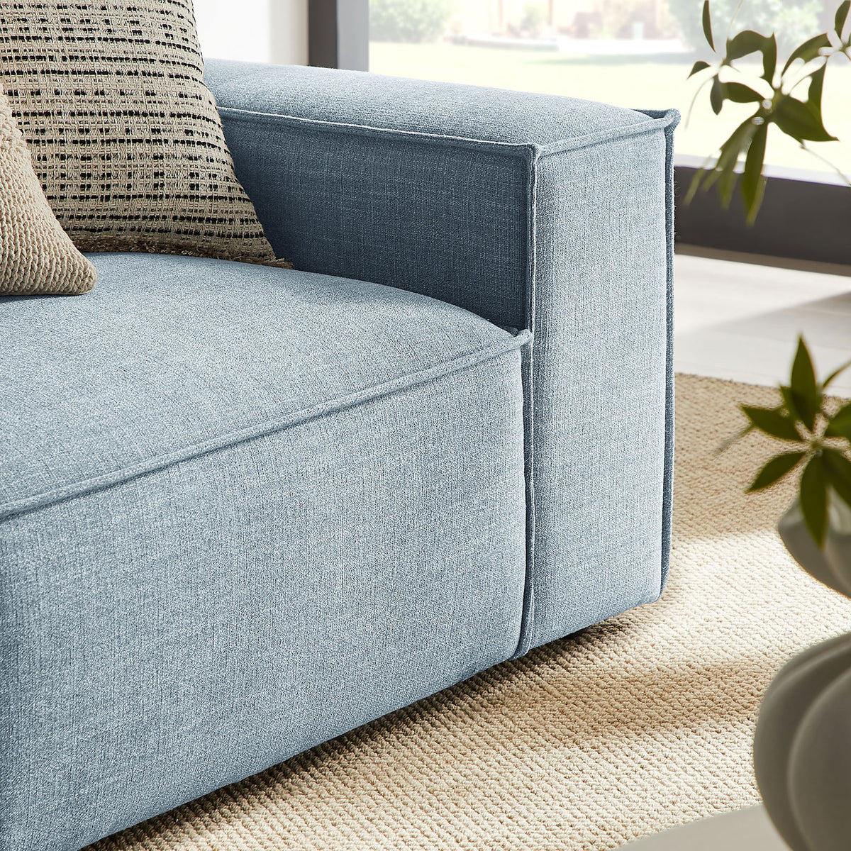 Boxy right armrest in sky blue fabric pairs with textured pillows to create a cozy, contemporary sofa corner || EEI-7427-SKY || detail_room