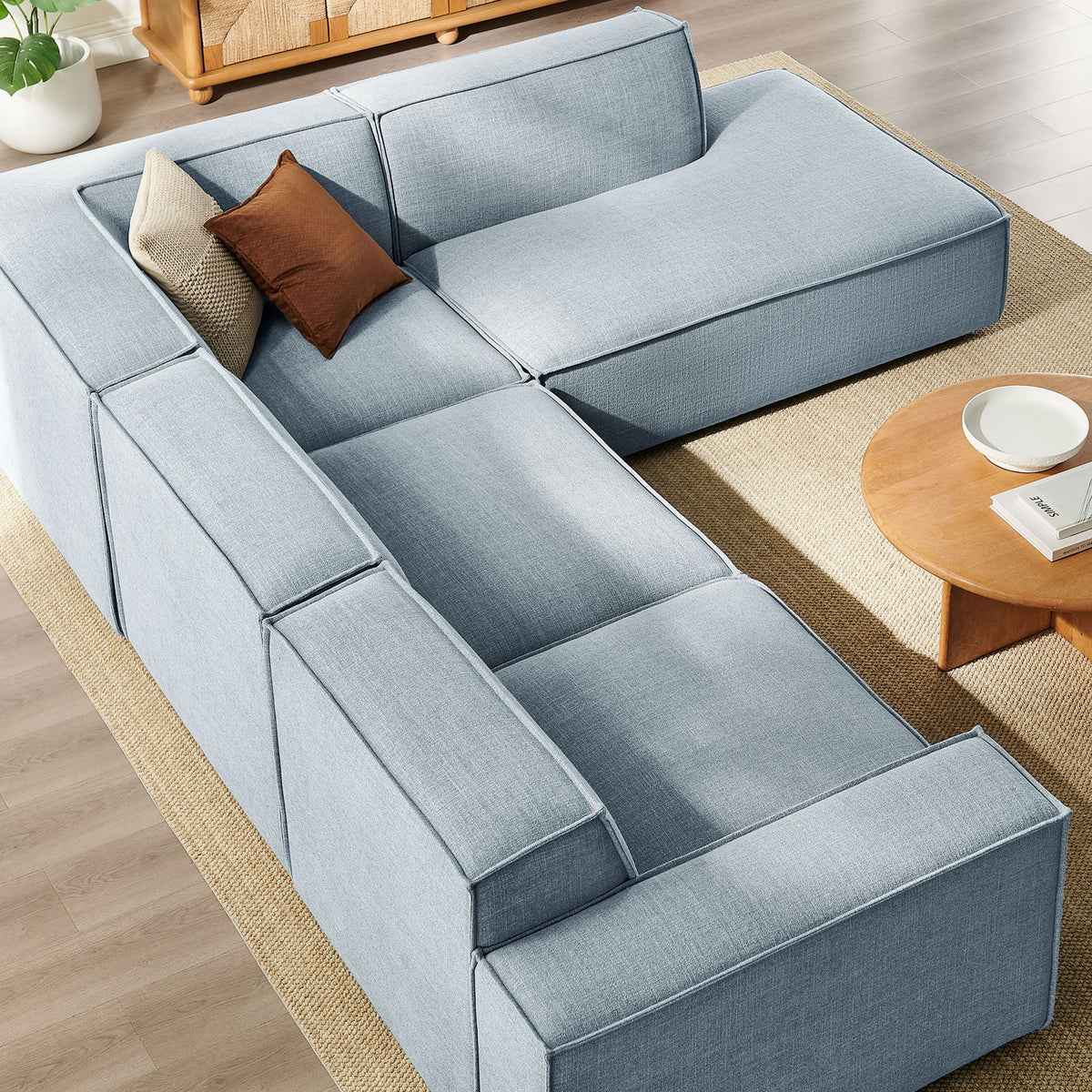 Sky blue L-shaped sectional arranged around a round wood coffee table on a neutral rug || EEI-7429-SKY || detail_room