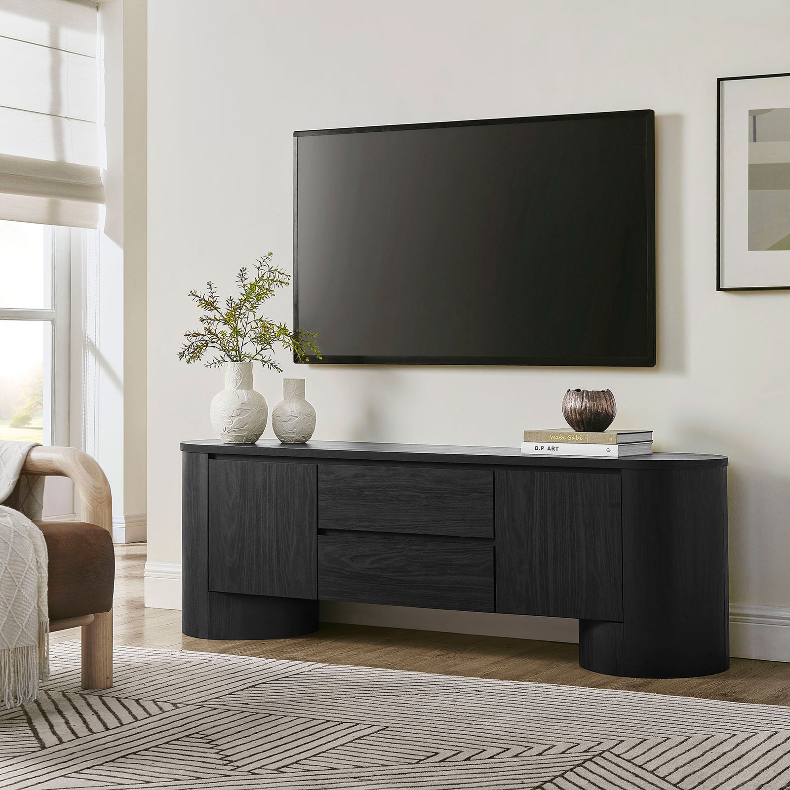 Black oval TV cabinet anchored beneath a wall-mounted screen in a bright modern living room || EEI-7440-BLK || front_angle_room