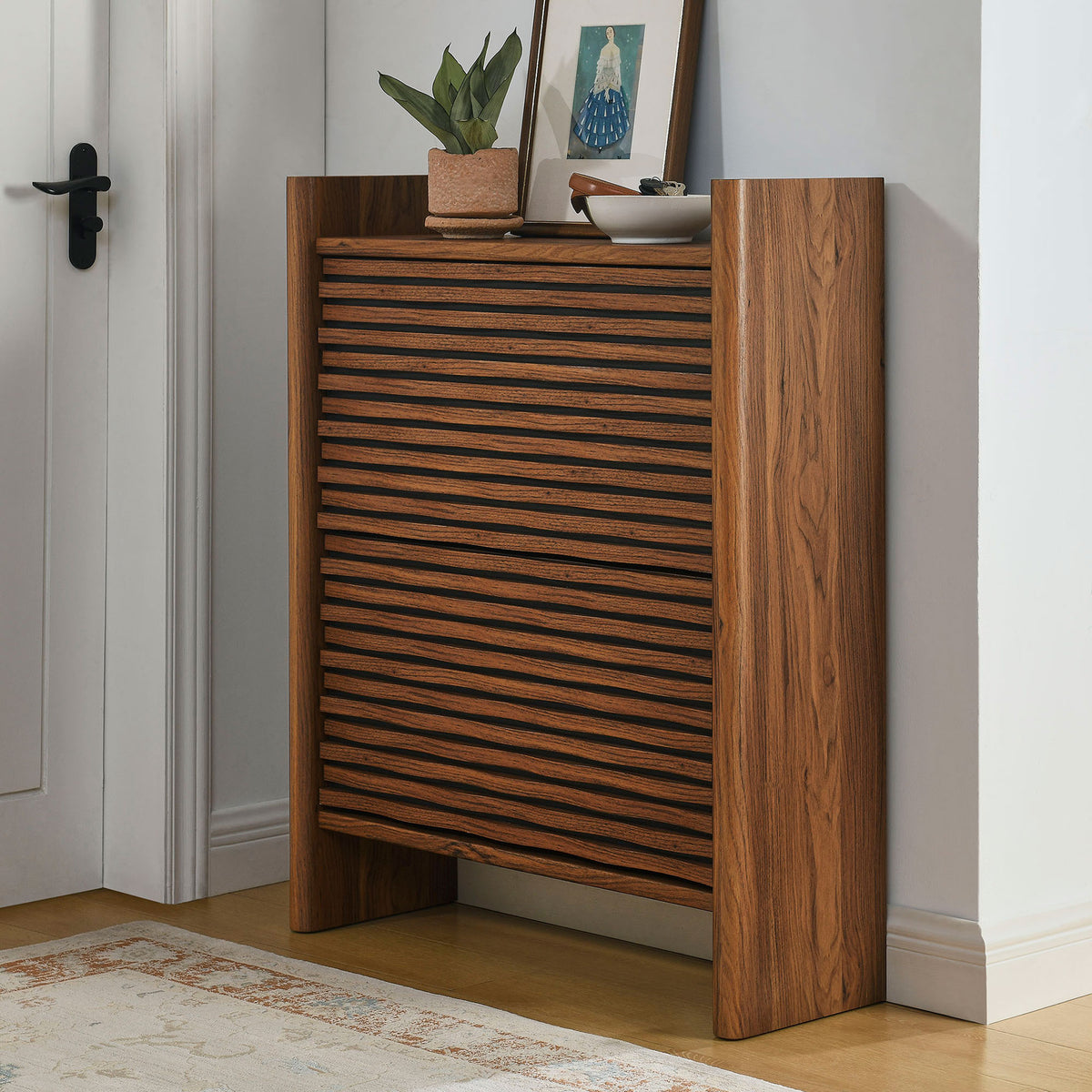 Walnut wave front shoe cabinet styled in an entryway with decor on the top and rug on the floor || EEI-7447-WAL || front_room