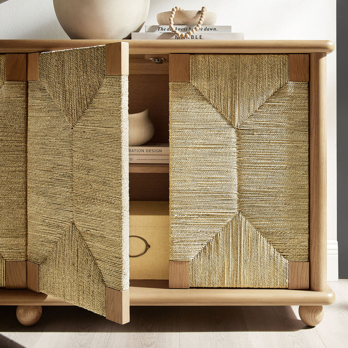 Seagrass doors partially open to reveal oak cabinet storage with styled books, boxes, and decor accents || EEI-7451-OAK || storage_open_room