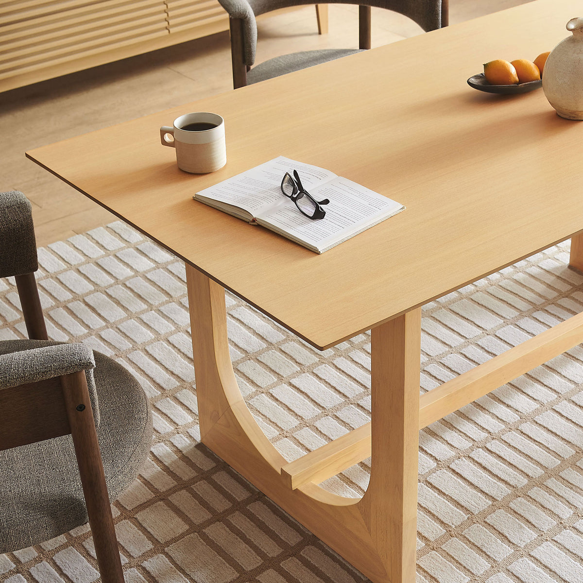 Dining table styled with book, mug, and decor to showcase the warm oak finish in use || EEI-7466-OAK || detail_room