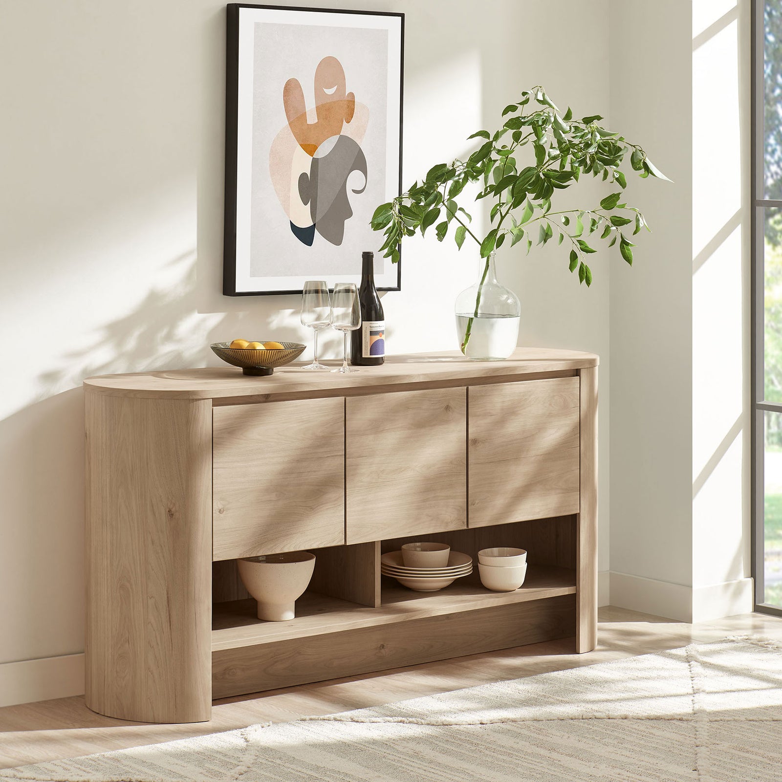 Oval sideboard styled in a bright living space with art, greenery, and entertaining essentials || EEI-7478-LOA || front_angle_room