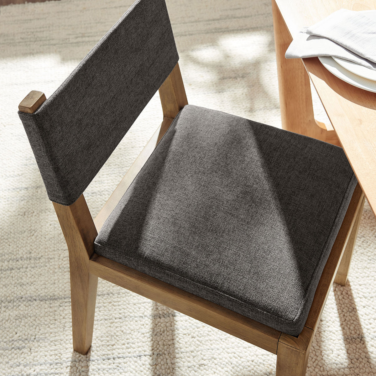 Dark gray cushioned seat and low backrest paired with a light wood table and textured area rug. || EEI-7485-HDG || detail_room