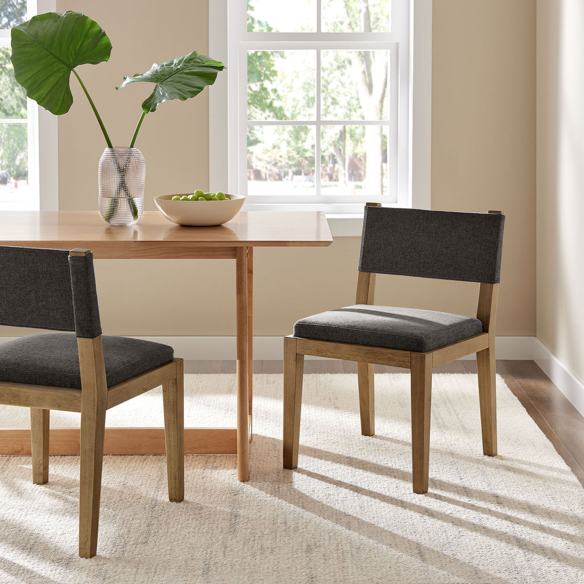 Dark gray upholstered dining chairs styled around a warm wood table in a bright, modern dining room. || EEI-7485-HDG || front_angle_room
