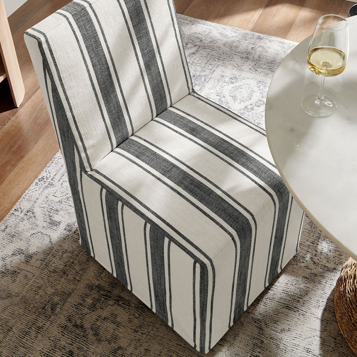 Striped slipcovered dining chair rolling easily into place beside a modern round dining table. || EEI-7486-BLK || front_angle_room