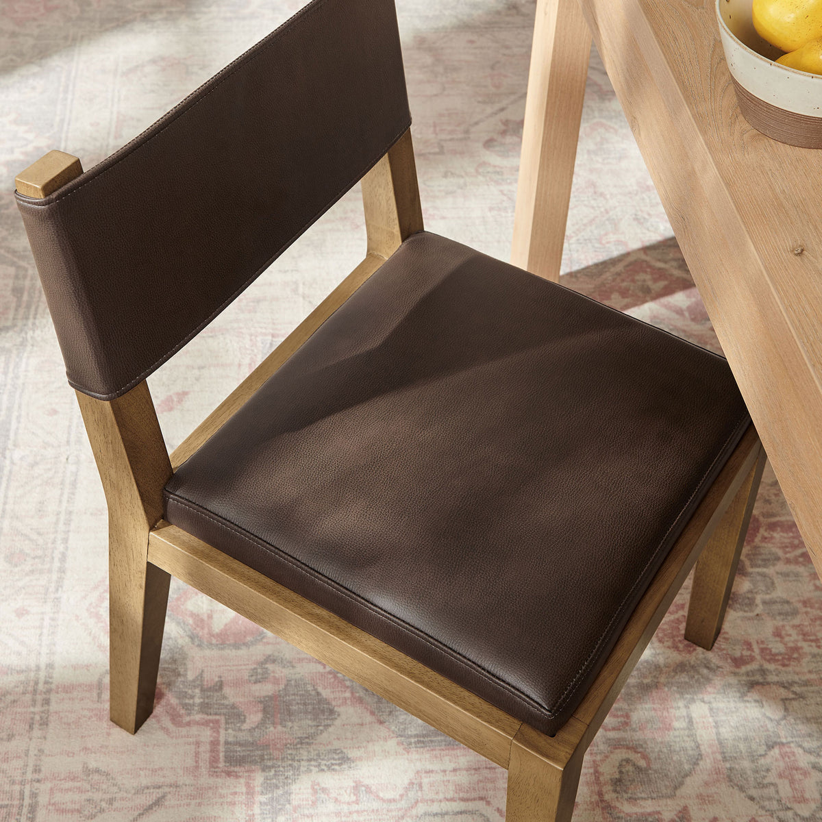 Calder dining chair beside a light wood table with espresso seat cushion over a softly patterned area rug || EEI-7527-ESP || top_angle_room