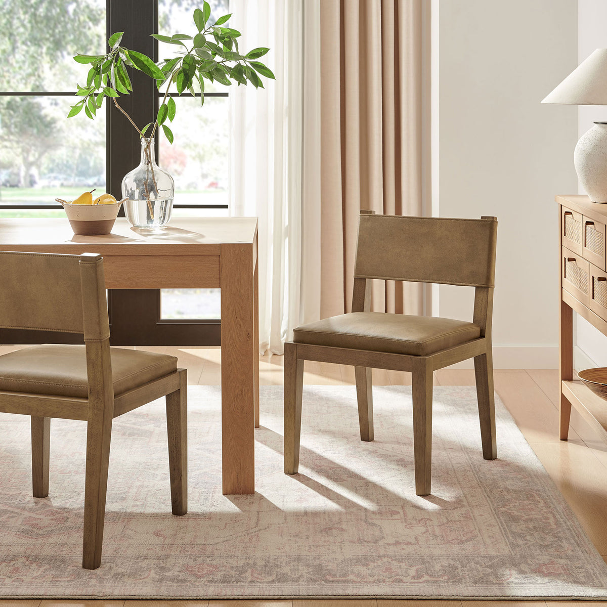 Pair of Calder toast vegan leather dining chairs in a bright dining room with wood table and matching sideboard || EEI-7527-TST || front_angle_room