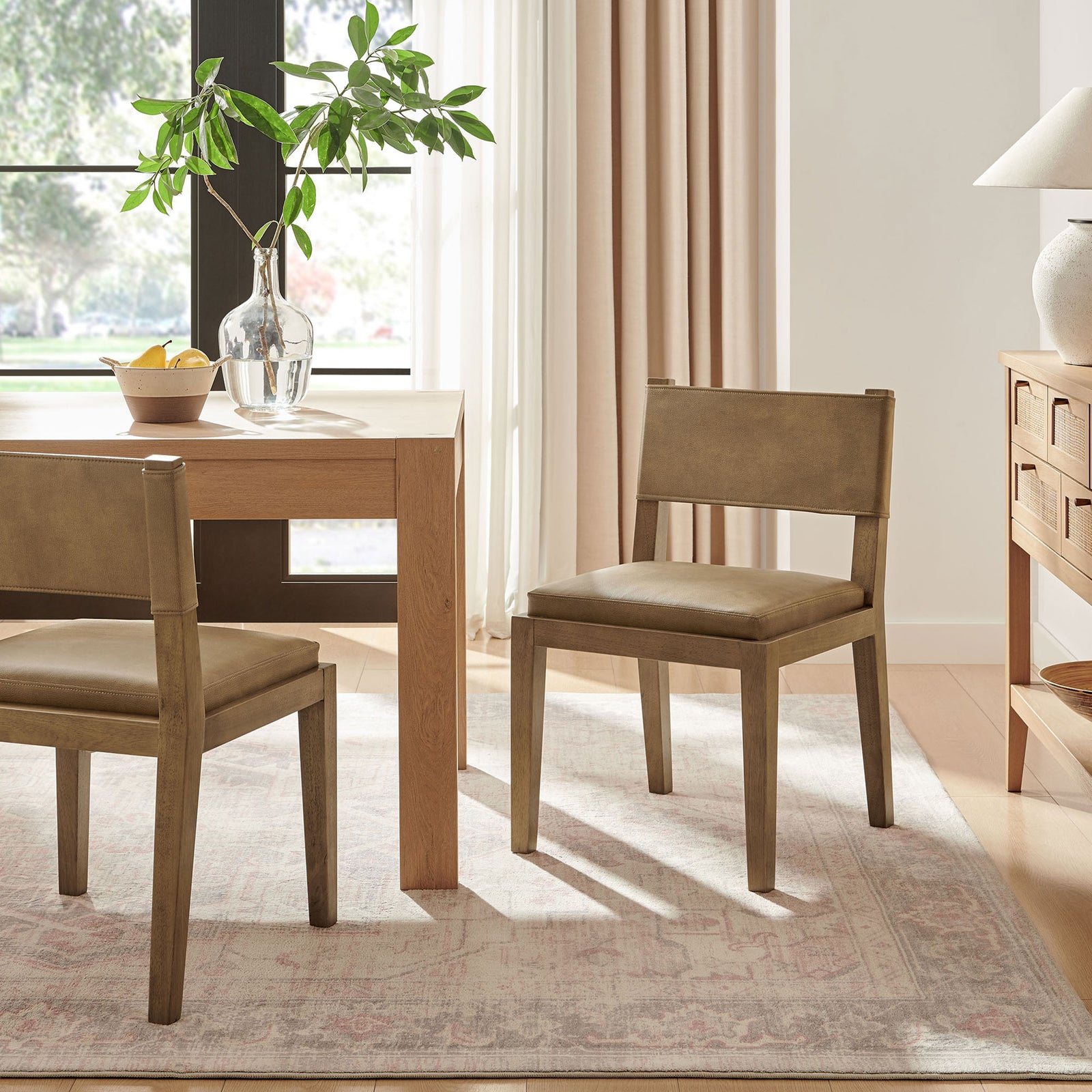 Pair of Calder toast vegan leather dining chairs in a bright dining room with wood table and matching sideboard || EEI-7527-TST || front_angle_room