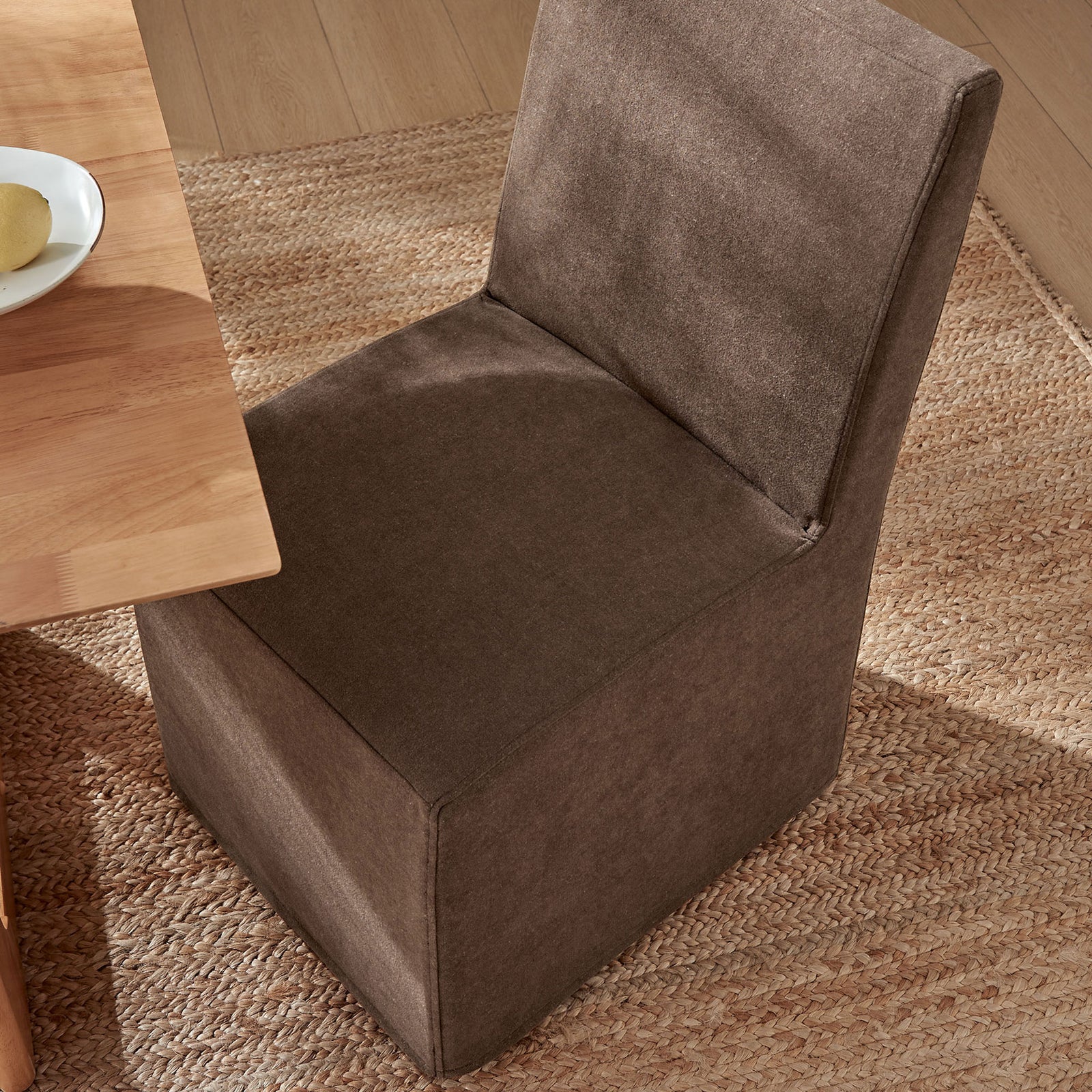 Cocoa slipcovered dining chair tucked at a wooden table on a textured jute rug for casual dining || EEI-7528-COA || top_angle_room