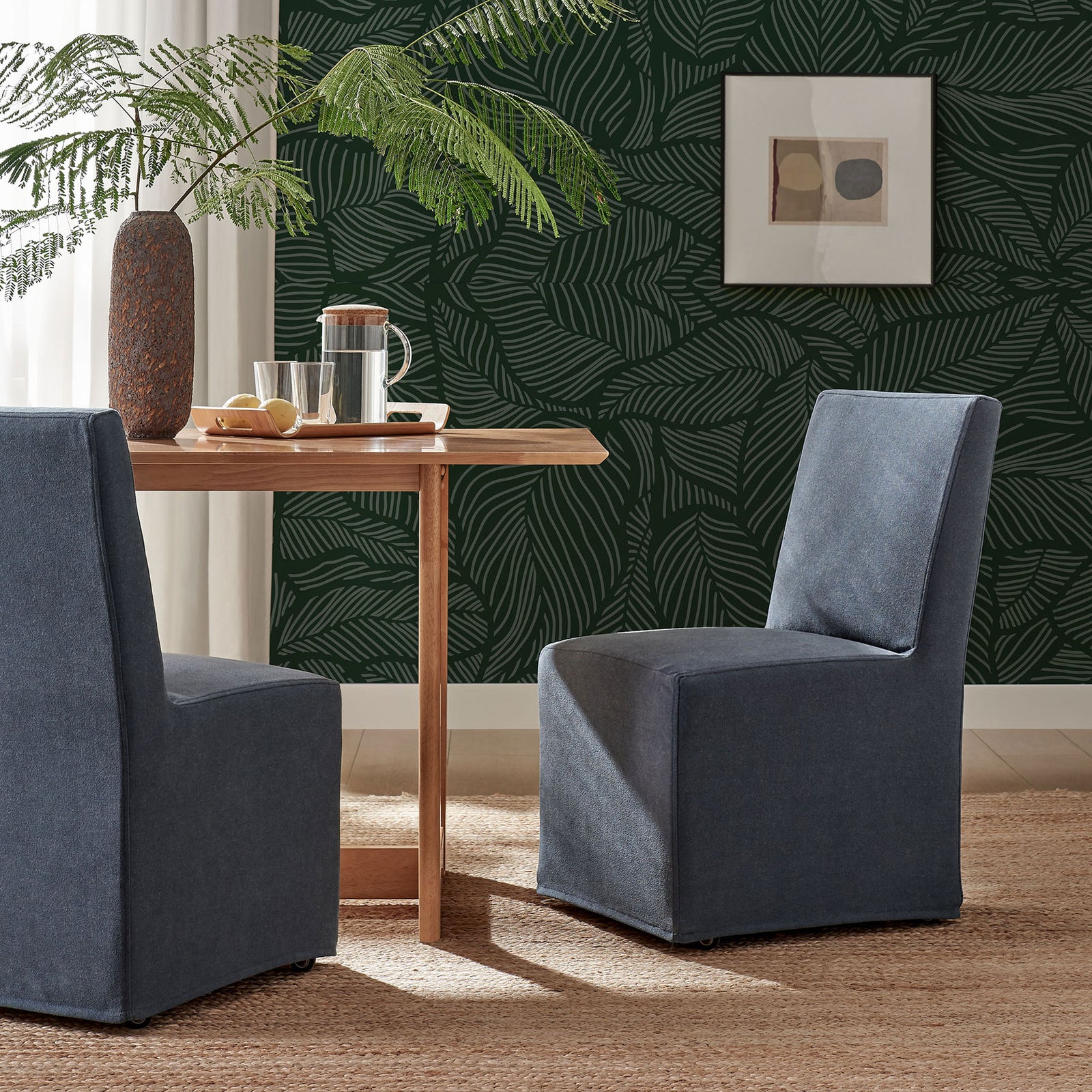 Two denim slipcovered dining chairs styled with a wood table in a leafy modern dining room || EEI-7528-DEN || front_angle_room