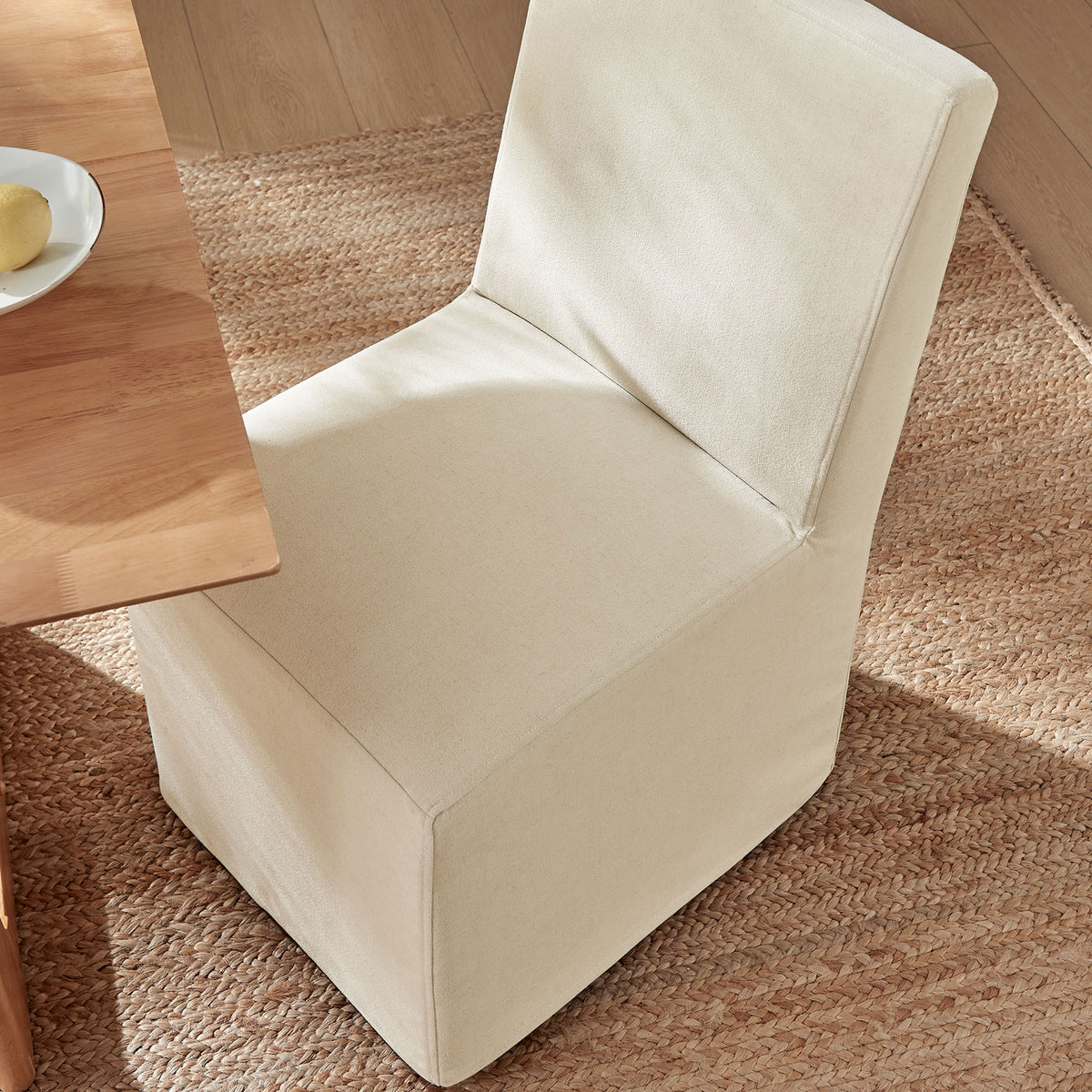 Slipcovered dining chair in a warm linen-blend fabric tucked neatly to a natural wood table on a woven rug. || EEI-7528-LIN || top_angle_room