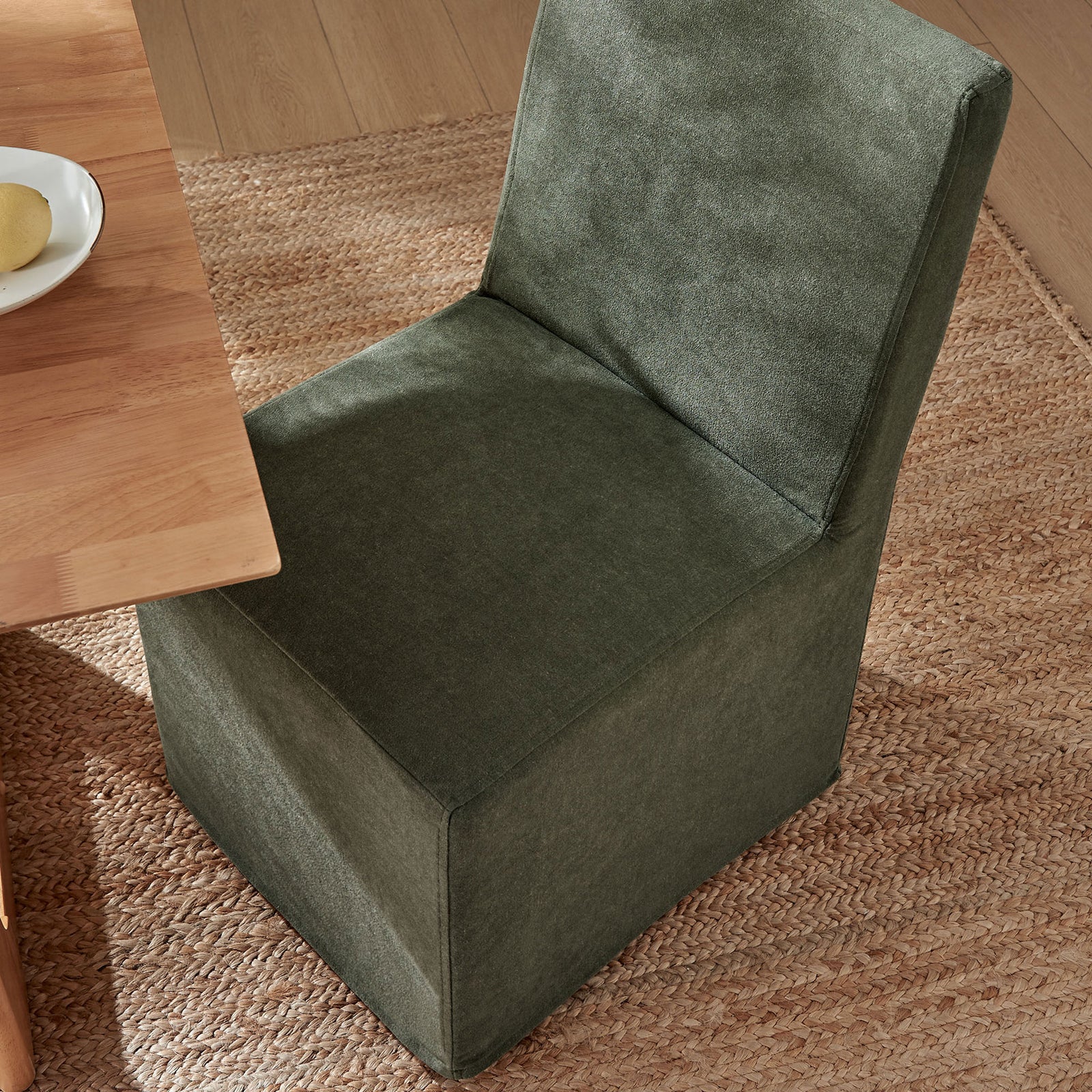 Slipcovered sage dining chair tucked under a warm wood table on a woven jute rug || EEI-7528-SGE || top_angle_room