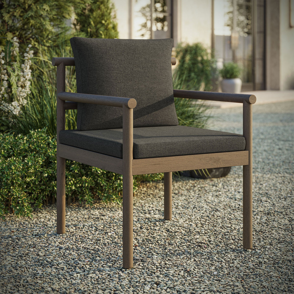 Gray teak outdoor chair with charcoal cushions styled on gravel terrace near greenery. || EEI-7561-WGR-FLI || front_angle_room