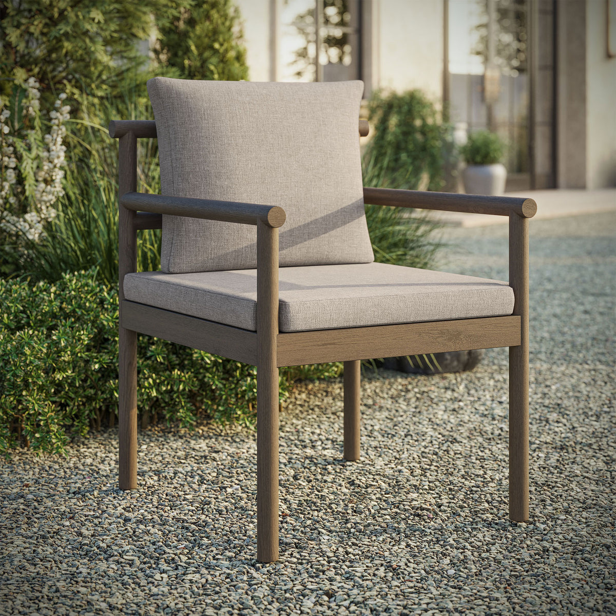 Gray teak outdoor dining chair with pebble cushions styled on gravel patio beside lush plants. || EEI-7561-WGR-PEB || front_angle_room