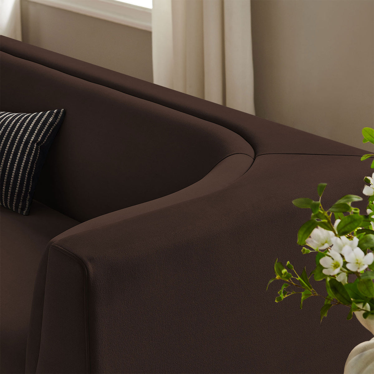 Velvet upholstery and curved arm of the Hilda sofa shown with layered pillows and fresh greenery in the room. || EEI-7564-CHB || detail_room