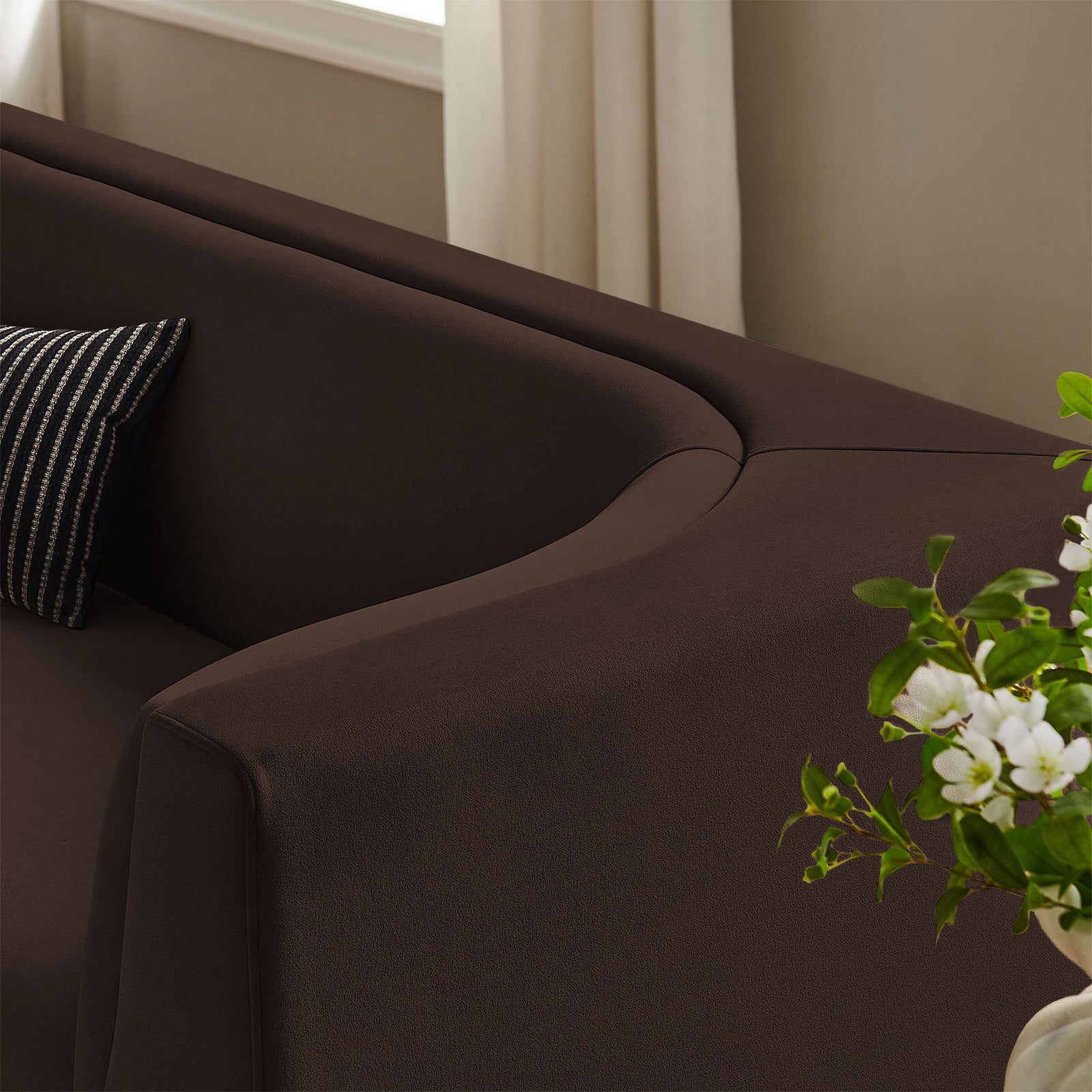 Velvet upholstery and curved arm of the Hilda sofa shown with layered pillows and fresh greenery in the room. || EEI-7564-CHB || detail_room